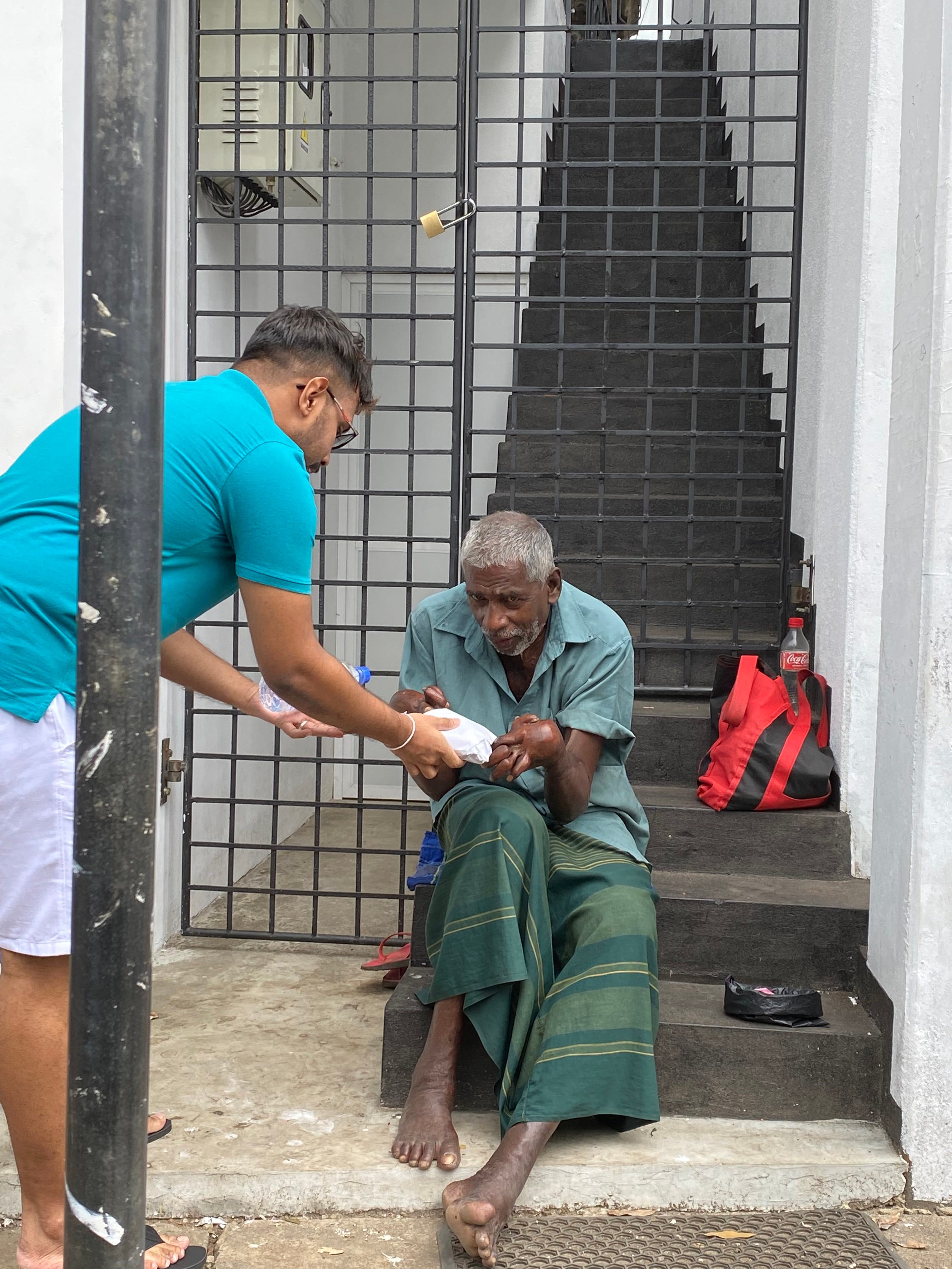 Ashan Veymont personally delivering food and water to an elderly man seated on steps